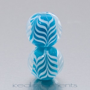May include: Two blue glass beads with a white swirl pattern. The beads are stacked on top of each other.