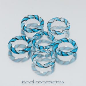 Pode incluir: Seis anéis de vidro listrados em azul e preto. Os anéis são de vidro transparente com um padrão listrado azul e preto.