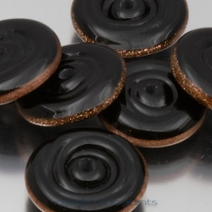 May include: Close-up of several black glass buttons with a spiral design. Each button has a bronze-colored, glittery edge. The buttons are arranged in a slightly overlapping pattern, showcasing their glossy surface.