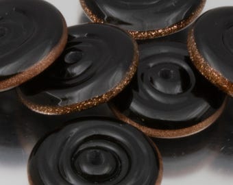 May include: Close-up of several black glass buttons with a spiral design. Each button has a bronze-colored, glittery edge. The buttons are arranged in a slightly overlapping pattern, showcasing their glossy surface.
