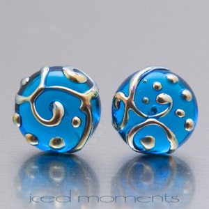 May include: Two round blue glass beads with gold swirls and dots. The beads are about 1 inch in diameter.