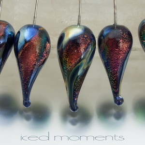 May include: Four iridescent glass teardrop ornaments with a blue, green, and gold color scheme. The ornaments are hanging from silver wires.