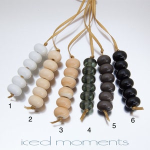 May include: Six strands of beads, each with a different color. The beads are strung on a brown cord. The colors are white, beige, light brown, green, gray, and black.