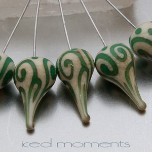 May include: Five green and white swirl patterned glass beads on silver pins. The beads are teardrop shaped and have a white background with green swirls.