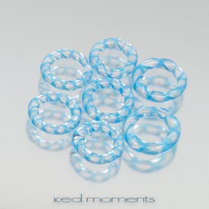 Pode incluir: Sete anéis de vidro transparente com um design de espiral azul claro. Os anéis estão dispostos em círculo.