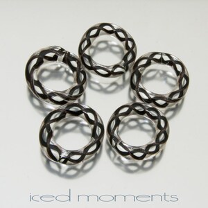 Pode incluir: Cinco anéis de vidro transparente com um design trançado preto. Os anéis são todos do mesmo tamanho e estão dispostos em círculo.