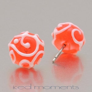 Könnte beinhalten: Ein Paar korallenrote Ohrstecker mit weißen Wirbelmustern. Die Ohrringe sind aus Polymer Clay gefertigt und haben einen Stiftverschluss.