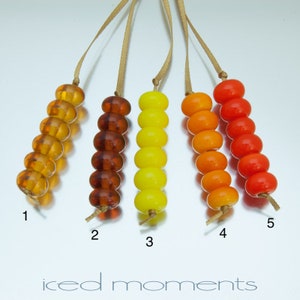 May include: Five strands of glass beads, each with a different color gradient. The beads are amber, brown, yellow, orange, and red. The beads are strung on a brown cord.