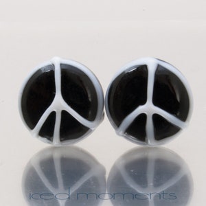 Op de afbeelding: Een paar zwarte en witte peace-teken oorbellen. De peace-tekens zijn gemaakt van glas en hebben een witte omtrek.