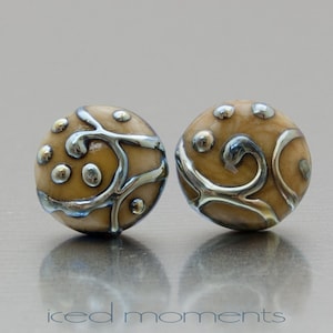 May include: A pair of small, round earrings with a beige background and silver swirls and dots.