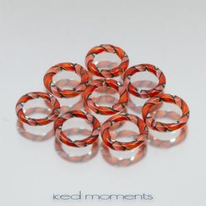 Pode incluir: Oito anéis de plástico laranja e preto com padrões, empilhados em forma de pirâmide. Os anéis são translúcidos e têm um acabamento brilhante.