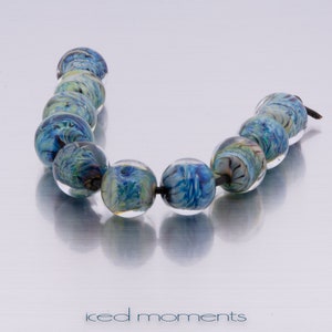 May include: A strand of blue and green glass beads with a swirling pattern. The beads are strung on a black cord.