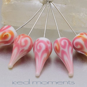 May include: Six pink and white swirl glass beads on silver pins. The beads are teardrop shaped and have a white background with pink swirls.
