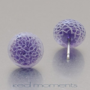 May include: A pair of purple glass earrings with a white swirl design. The earrings are stud style with silver posts.