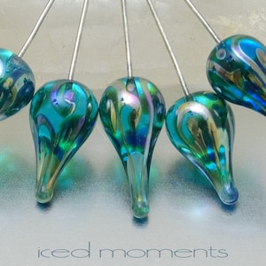 May include: Six teal blue glass teardrop-shaped beads with iridescent gold and green swirls on silver pins.