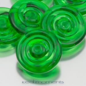 May include: Close-up of several green glass buttons with a spiral design. The buttons are shiny and reflect light.