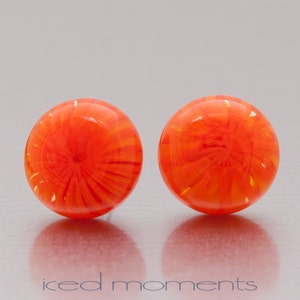 Könnte beinhalten: Ein Paar orangefarbene Glasohrringe mit einem wirbelnden Muster. Die Ohrringe sind rund und haben eine glänzende Oberfläche.