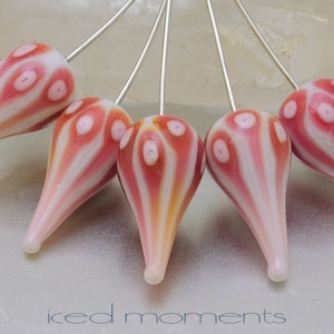 May include: Five teardrop-shaped glass beads with a white and pink swirl pattern and white polka dots. The beads are strung on silver wires.