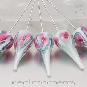 May include: Six glass flower pins with silver stems. The glass is white with pink and green swirls and a pink flower design.