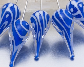 Könnte beinhalten: Nahaufnahme von mehreren blau-weißen Glasornamenten in Tropfenform. Jedes Ornament hat einen silbernen Draht und ein wirbelndes weißes Muster auf blauem Hintergrund. Der Text "iced moments" ist unten zu sehen.