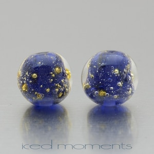 May include: Two blue glass beads with gold flecks and air bubbles inside. The beads are round and have a glossy finish.