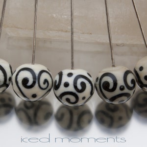 May include: A strand of white beads with black swirl designs. The beads are strung on silver wires.