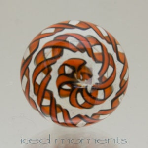 Könnte beinhalten: Ein Glas-Briefbeschwerer mit einem wirbelnden orange-weißen Muster. Das Muster ähnelt einem geflochtenen Zopf.