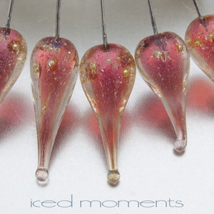 May include: Six teardrop-shaped glass ornaments with gold flecks and a pink hue, suspended on silver wires.