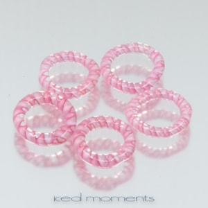 Pode incluir: Cinco anéis de vidro rosa com um padrão de espiral. Os anéis são translúcidos e têm um acabamento brilhante.