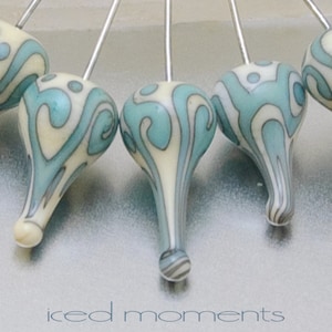 May include: A set of six blue and white swirl glass beads on silver pins. The beads are teardrop shaped and have a white background with blue swirls.