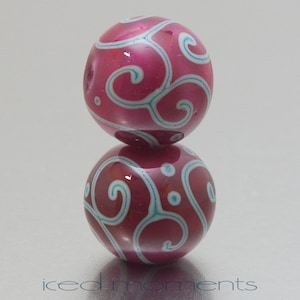 May include: Two pink glass beads with a white swirl design. The beads are stacked on top of each other.