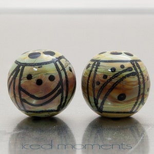 May include: Two round, ceramic beads with a brown, green, and black geometric pattern. The beads have a glossy finish.