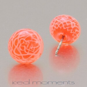 Könnte beinhalten: Ein Paar pfirsichfarbene Ohrstecker mit einem zarten weißen Spitzenmuster. Die Ohrringe haben silberne Stiele.