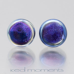 May include: A pair of iridescent blue and purple glass earrings. The earrings are round and have a textured surface.