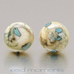 May include: A pair of round, white earrings with blue and brown swirls and speckles.