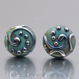 May include: A pair of teal blue and silver earrings with a swirl design and silver dots. The earrings are round and have a glossy finish.