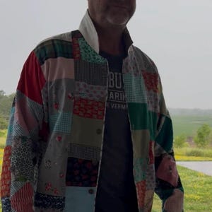 May include: A patchwork jacket constructed from various fabric squares featuring diverse patterns including floral, plaid, gingham, and solid colors in shades of red, green, blue, and white. The jacket has a high collar, a button-front closure, and long sleeves.