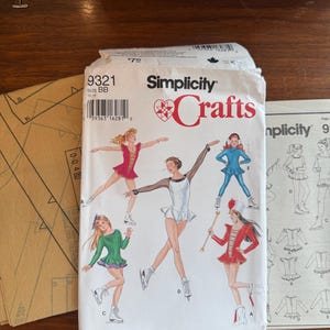 May include: A Simplicity Crafts sewing pattern envelope, number 9321, size BB, featuring illustrations of five figures in various skating and performance outfits, including dresses and leggings, with accompanying paper pattern pieces and instruction sheets.