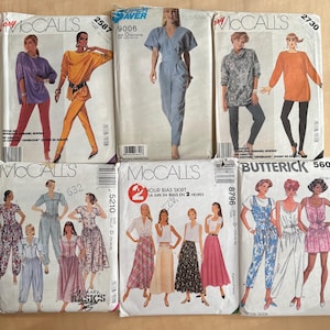 May include: A collection of six vintage sewing pattern envelopes from McCall's and Butterick brands. The paper envelopes feature illustrations of various clothing styles including jumpsuits, skirts, tunics, and trousers with printed model images.