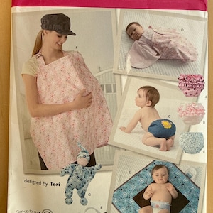 May include: Simplicity sewing pattern 2165 featuring baby items. The pattern includes a nursing cover, baby blanket, diaper covers, and a baby doll. The cover and blanket have a pink floral pattern. The pattern is designed by Teri.