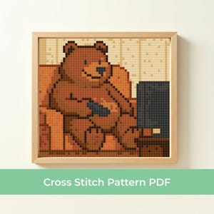 May include: A framed cross-stitch pattern depicts a brown bear relaxing on a brown couch, holding a remote control, and watching a black television. The bear is smiling. The background is a pixelated beige and brown pattern. The text "Cross Stitch Pattern PDF" is at the bottom.