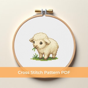 Puede incluir: Un patrón de punto de cruz de una oveja en un bastidor de bordado de madera. La oveja es de color beige claro con un poco de hierba verde a sus pies. El texto "Cross Stitch Pattern PDF" se muestra en una pancarta horizontal naranja.