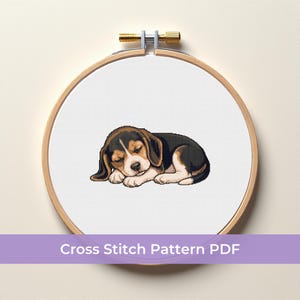 Könnte beinhalten: Ein Kreuzstichmuster mit einem schlafenden Beagle-Welpen. Der Welpe ist in Schwarz, Braun und Weiß dargestellt und ruht auf einem weißen Hintergrund in einem hölzernen Stickrahmen. Der Text "Cross Stitch Pattern PDF" wird auf einem lila Banner angezeigt.