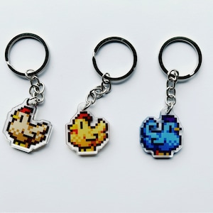 May include: Three keychains featuring pixelated animal designs. One keychain has a yellow chicken, another a white chicken, and the third a blue bird.