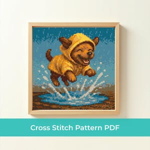 May include: A framed cross-stitch pattern of a happy brown puppy wearing a yellow raincoat and hood, jumping in a puddle. The background is blue with a pixelated effect, and the frame is light brown.