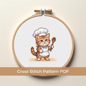 Puede incluir: Patrón de punto de cruz con un gato chef de dibujos animados con gorro y delantal blancos, sosteniendo una cuchara de madera. El gato es marrón y blanco, sobre un fondo blanco dentro de un bastidor de bordado de madera. El texto "Cross Stitch Pattern PDF" está en la parte inferior.