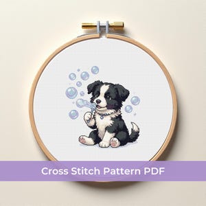 May include: A cross-stitch pattern featuring a black and white puppy blowing bubbles. The puppy is sitting inside a wooden embroidery hoop. The text "Cross Stitch Pattern PDF" is displayed on a purple banner at the bottom.