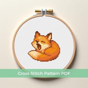 Könnte beinhalten: Ein Kreuzstichmuster eines gähnenden Fuchses in Orange- und Brauntönen, in einem hölzernen Stickrahmen. Der Text "Cross Stitch Pattern PDF" ist unterhalb des Rahmens zu sehen.