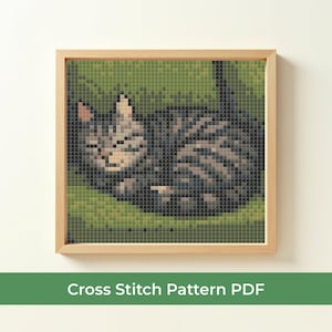 Könnte beinhalten: Ein gerahmtes Kreuzstichmuster einer schlafenden getigerten Katze. Die Katze ist in Grau- und Brauntönen dargestellt und liegt auf einem grünen Hintergrund. Der Rahmen ist aus hellem Holz. Der Text unten lautet "Cross Stitch Pattern PDF".