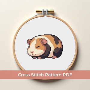 Puede incluir: Un patrón de punto de cruz de un conejillo de indias pixelado, dentro de un aro de bordado de madera. El conejillo de indias es marrón, beige y negro. El texto "Cross Stitch Pattern PDF" se muestra debajo.